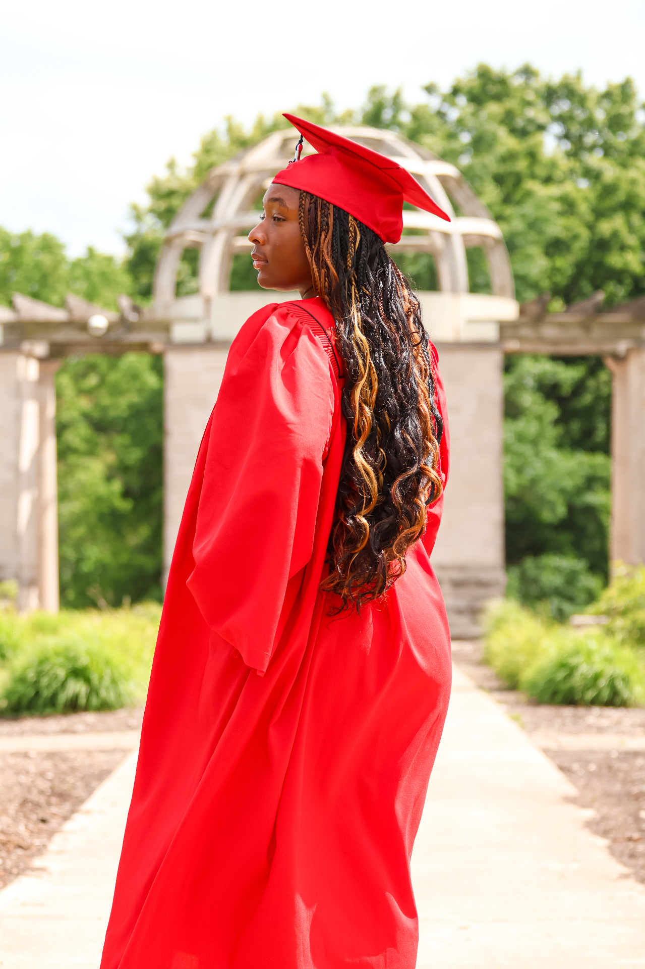 Senior in red gown at garden arch